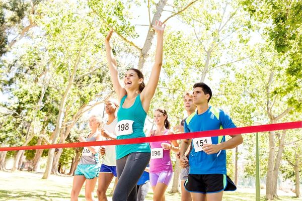 A runner crossing the finish line of a marathon with arms raised in celebration.
